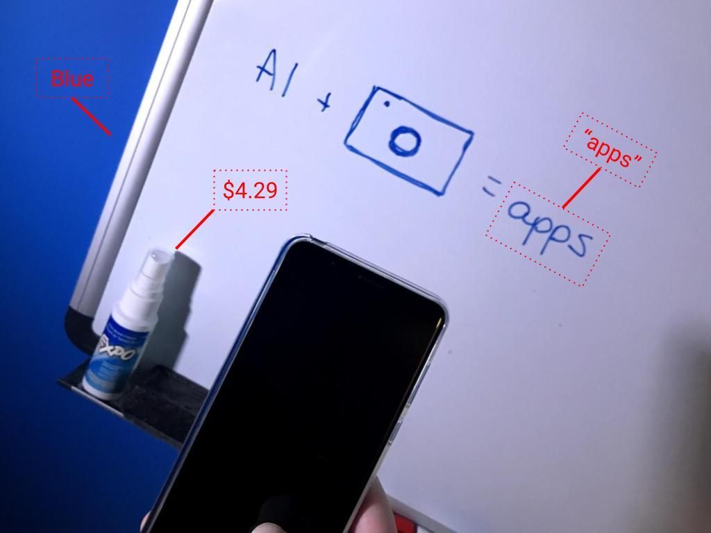Photo of smartphone camera point at a white dry erase board, a blue wall, marker cleaner bottle, writing "AI + (image of camera) = apps"; red line link objects to information (from bottle to a price, from word apps to "apps"; from wall to "Blue")